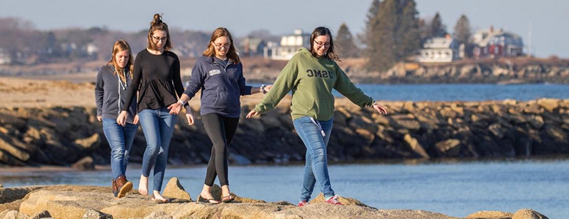 四个学生沿着海岸在岩石上行走